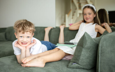 Naeratav poiss ja tüdruk puhkavad koos diivanil, tüdruku käes on tahvelarvuti ALPA Kidsi rakendusega.